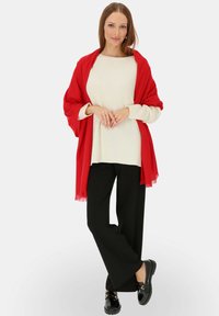 Czerwona chusta na kremowym swetrze, połączona z czarnymi szerokimi spodniami i czarnymi loafersami. Gładka faktura z frędzlami na chustie.