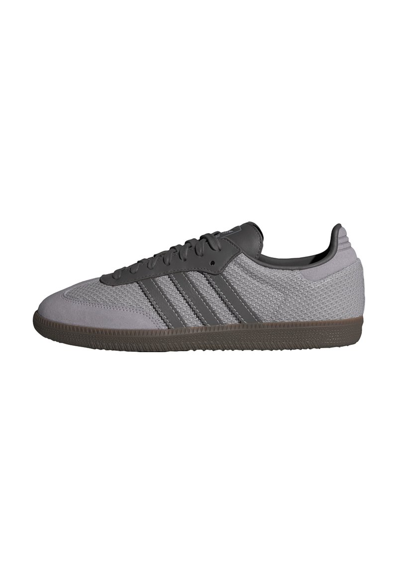 Grå atletisk sko med texturerad mesh-övre, mörkgrå läderdetaljer, tre ränder och gummisula. Klassisk lågprofildesign.