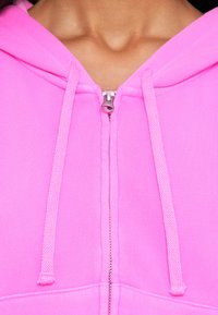 Felpa fucsia con zip, caratterizzata da una cerniera frontale, cappuccio regolabile e una morbida texture di tessuto. Accentuata da dettagli metallici sulla zip.