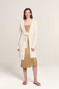 Cremfarbener, gestrickter Cardigan mit offenem Front und Taillengürtel, kombiniert mit einem fließenden goldenen Satin-Nachthemd. Flache, gewebte Sandalen.