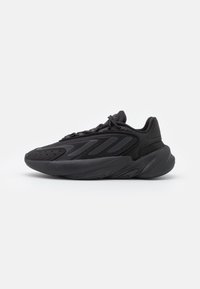 Sneaker atletica nera con tomaia in tessuto liscio e elementi di design a strati, suola intermedia arrotondata e suola in gomma testurizzata.