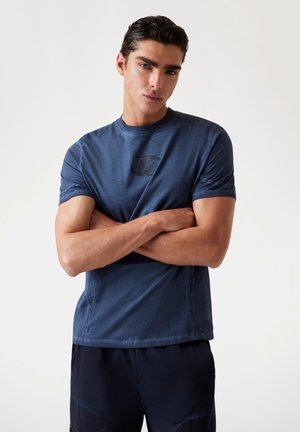Tricou bleumarin cu mânecă scurtă, având un guler rotund și un logo embosat pe piept. Materialul pare neted, cu o textură subtilă.