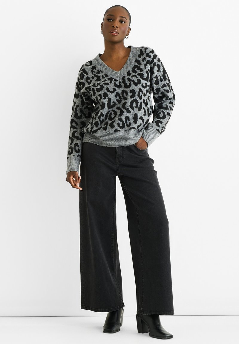 Grauer V-Ausschnitt-Pullover mit schwarzem Leopardenmuster, gerippten Bündchen und Saum. Kombiniert mit schwarzen weiten Jeans und schwarzen Stiefeletten mit Absatz.