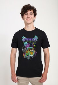 Schwarzes Baumwoll-T-Shirt mit einem bunten "Scooby-Doo"-Motiv, das Figuren in einem Cartoon-Auto zeigt, umgeben von geisterhaften und gruseligen Elementen.