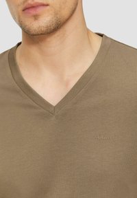 Zielono-oliwkowa koszulka z dekoltem w serek, wykonana z gładkiej bawełny, z logo s. Oliver w kontrastującym beżowym kolorze po lewej stronie.