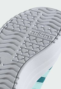 Ljust grå sneakersula med ett texturerat mönster, med en präglad "adidas"-logotyp och turkosa accenter längs sidorna.