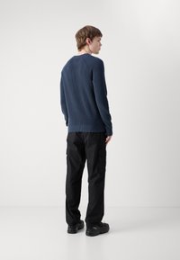 Maglione a righe blu navy con scollatura tonda, abbinato a pantaloni cargo neri. L'outfit presenta maniche lunghe e una finitura testurizzata.