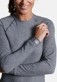 Maglietta grigia a maniche lunghe con tessuto testurizzato, caratterizzata da un colletto arrotondato e una vestibilità attillata. Le cerniere presentano un piccolo logo ricamato.