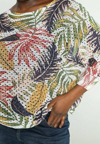 Top ligero de manga corta con un patrón colorido de hojas en rojo, verde y amarillo sobre un fondo blanco perforado.