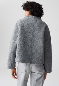Giacca cropped in lana grigia con finitura testurizzata, maniche larghe e colletto alto, caratterizzata da un dettaglio di cucitura dritta sul retro.