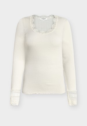 Bijela rebrasta majica dugih rukava s čipkanim obrubom na izrezu i manžetama, uskog kroja i lagane tkanine.