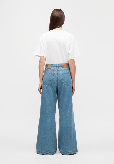 Φαρδιά τζιν παντελόνια σε ανοιχτό μπλε με ψηλή μέση και λεπτομέρειες με τσέπες. Συνδυασμένα με απλό λευκό κοντομάνικο μπλουζάκι.