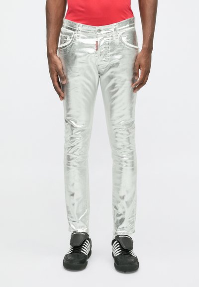 Metallik hõbedased teksad slim-fit lõikega, viie taskuga ja kontrastsete õmblustega, kombineerituna mustade tossudega, millel on valged triibud.