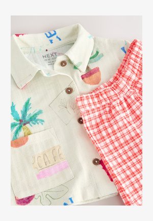 Kortärmad skjorta med knappar i ljus beige med färgglada växtmotiv och en bröstficka, kombinerad med röd- och vitrutiga shorts.