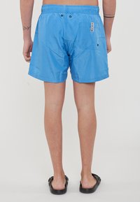 Pantaloni da bagno blu realizzati in materiale leggero, con vita elastica, tasche laterali e un'etichetta sul retro. Texture liscia.