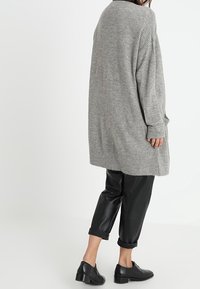 Grå stickad kofta med lös passform, långa ärmar och ribbade detaljer, kombinerad med svarta läderbyxor och svarta skor.