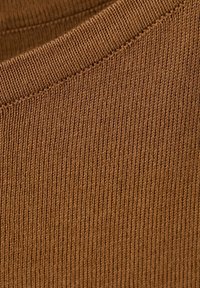 Zbliżenie brązowej dzianiny z widoczną prążkowaną fakturą i szwem biegnącym ukośnie przez kadr.