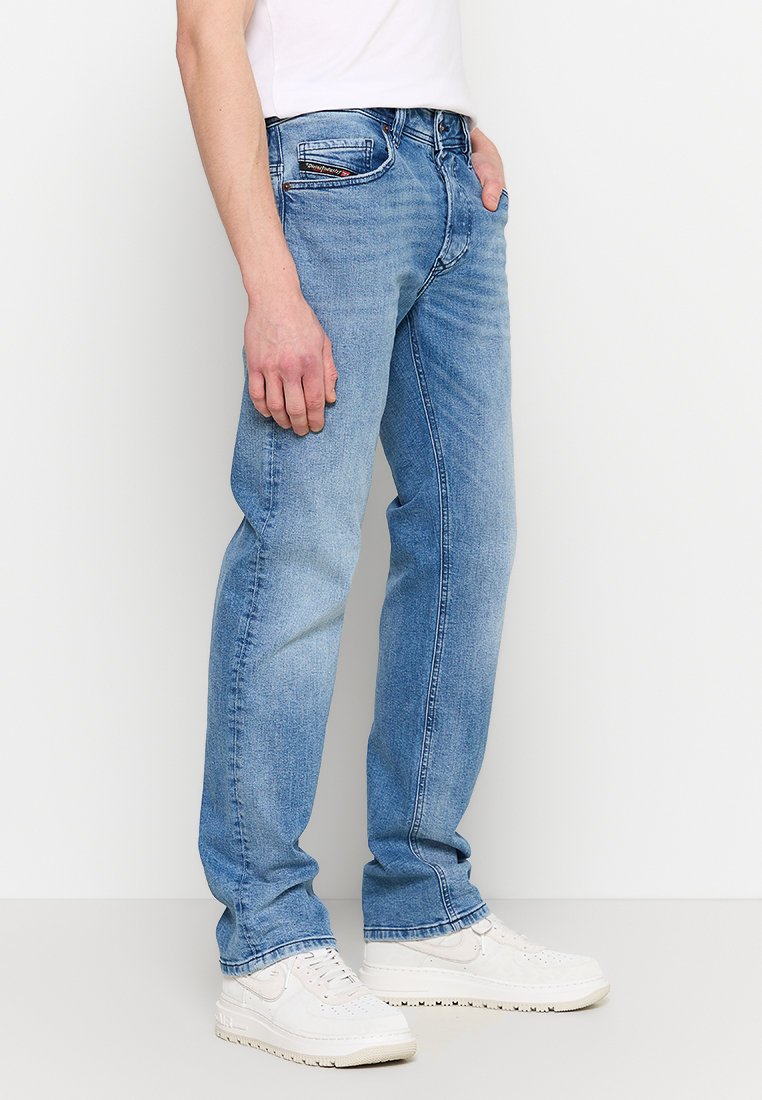Jean en denim bleu clair avec une coupe droite, design à cinq poches et un petit logo sur la poche avant, associés à des baskets blanches.