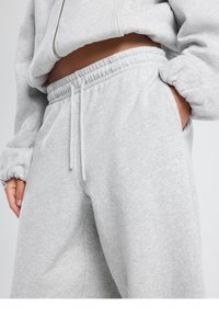 Vaaleanharmaat collegehousut pehmeästä kankaasta, joissa joustava vyötärönauha, kiristysnauha ja sivutaskut. Hienovarainen logoyksityiskohta lähellä lahkeenreunaa.