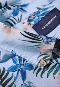 Bloemige overhemd met knopen in lichtblauwe katoen, voorzien van blauwe en crème bloemen met groene bladeren, en een LINDBERGH-label bij de kraag.