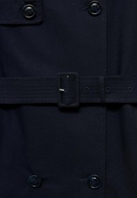 Tmavě modrá trench coat látka s černými knoflíky a páskem ze stejného materiálu s obdélníkovou sponou umístěnou vpředu na pase.