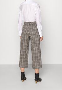 Bruna rutiga cropped-byxor i bomull med hög midja, bakfickor och raka ben, i kombination med svarta ankelstövlar.