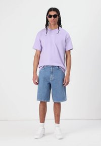 Light purple cotton t-shirt with short sleeves, paired with light blue denim shorts. White sneakers and black sunglasses complete the look.