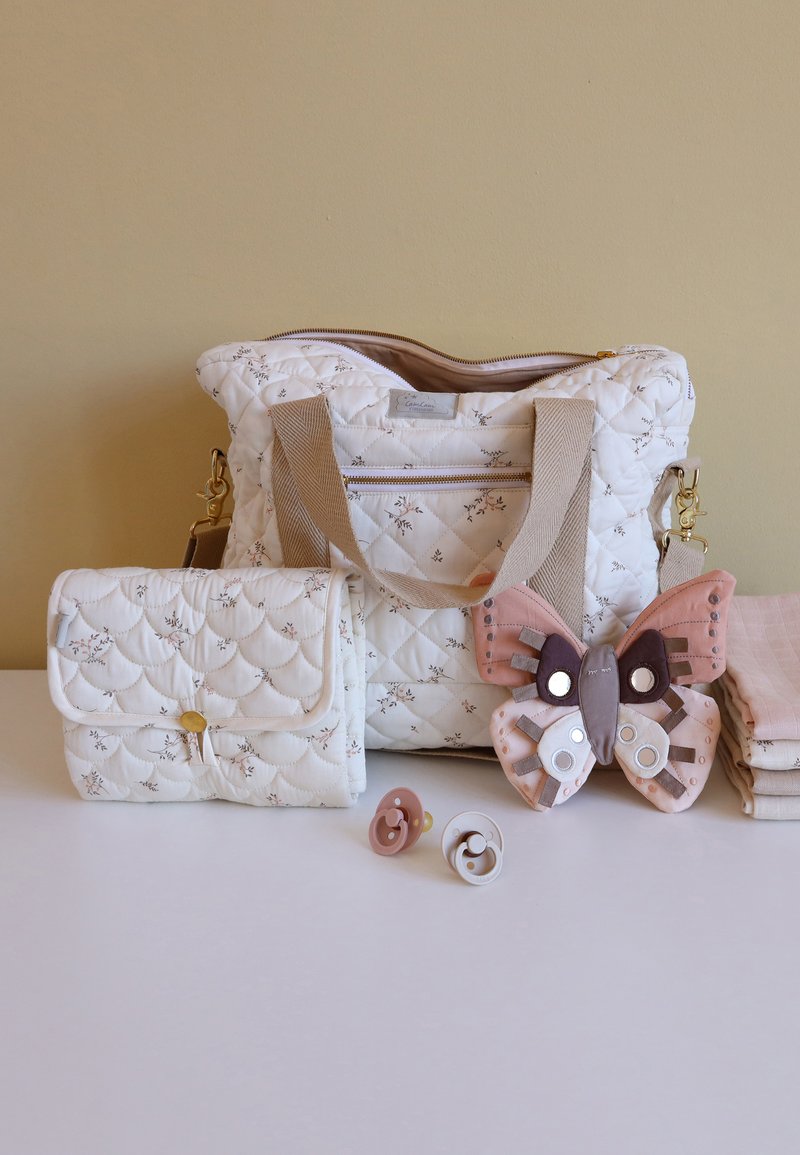 Quilted cream diaper bag with floral pattern and beige straps, a smaller matching pouch, a butterfly toy, and two pacifiers in pink and white.