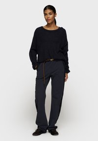 Maglione nero a maglia con scollatura ampia abbinato a pantaloni in nylon grigio scuro con una striscia laterale e vita arricciata con una cintura marrone.
