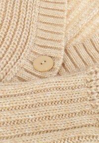 Beige gebreide stof met ribbel- en textuurpatronen, met een beige knoop met twee gaten genaaid op het materiaal.