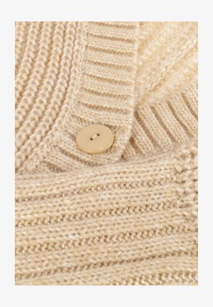 Beige gebreide stof met ribbel- en textuurpatronen, met een beige knoop met twee gaten genaaid op het materiaal.