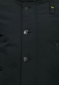 Svart jacka med dragkedja och knappstängning, med glänsande svarta knappar, en slät textur och framfickor.