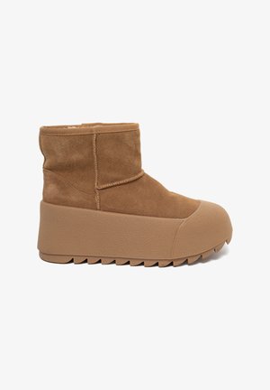 Brązowy zamszowy botek za kostkę z grubą teksturowaną podeszwą, okrągłym nosem i przeszyciami po bokach.