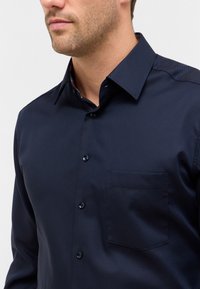 Marineblauwe button-up overhemd met een gestructureerde afwerking, voorzien van een zak aan de linkerborst en contrasterende details aan de binnenkant van de kraag.