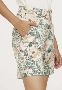 Shorts à motifs floraux fabriqués à partir d'un tissu léger, présentant un fond crème doux, des feuilles vertes et des fleurs beiges. Comprend des poches latérales.