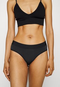 Zwarte draadloze bralette met een V-hals en geribbelde structuur; gecombineerd met bijpassende zwarte high-waisted slips met een gladde tailleband.
