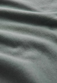 Tejido suave y texturizado en un color gris apagado, con suaves ondas y pliegues que destacan su superficie lisa y su patrón tejido.