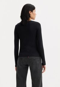 Chemise noire à manches longues en coton lisse, avec un design ajusté, un décolleté rond et une étiquette de marque discrète à l'ourlet.