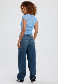 Light blue fitted lace top with short sleeves, paired with loose dark blue denim jeans, featuring a classic five-pocket design.