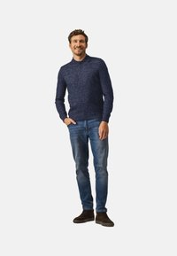 Marineblauw gebreid trui met een kraag en drie knopen, gedragen met lichtblauwe spijkerbroek en donkerbruin gestructureerde schoenen.