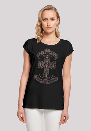 Schwarzes T-Shirt mit kurzen Ärmeln, das ein grafisches Design eines Totenkopf- und Kreuzmotivs mit dem Text "GUNS N' ROSES" und "APPETITE FOR DESTRUCTION" zeigt.