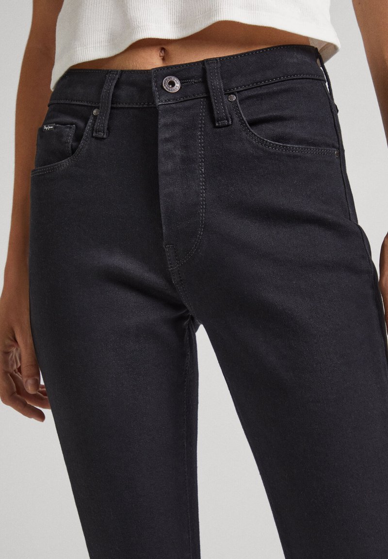 Schwarze Jeans aus Denim mit hohem Bund, figurnaher Silhouette, Fünf-Taschen-Design und kontrastierenden Nähten. Metallknopfverschluss am Bund.