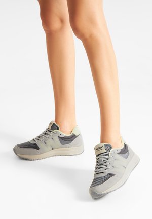 Gray athletic shoes with mesh and suede materials. Features a textured sole, light green accents, and gray laces. Woden logo on heel.