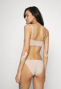 Beige naadloze bralette met verstelbare bandjes, gecombineerd met bijpassende bikini-achtige broekjes. Zachte textuur en minimalistisch ontwerp.