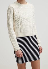 Kermanvärinen neulottu villapaita, jossa on kuvioituja pintoja, yhdistetty mustavalkoraidalliseen hameeseen, jossa on vartaloa myötäilevä malli.