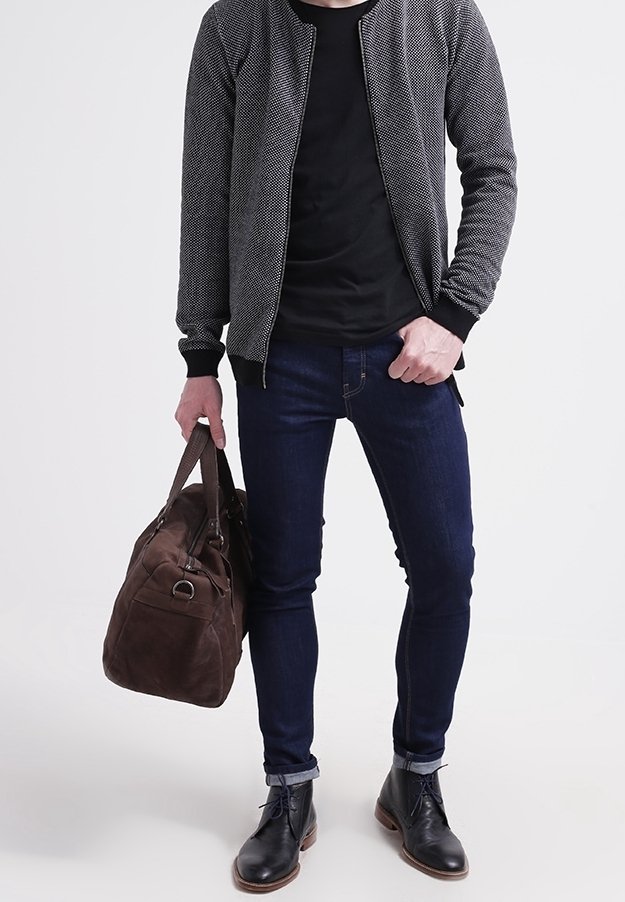 Svart bomberjacka med texturerat tyg, svart t-shirt, mörka jeans, brun mocka duffelväska och svarta läderstövlar.