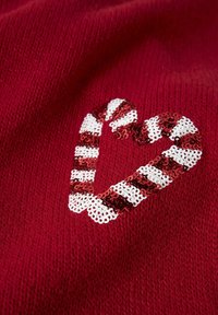 Tejido de punto rojo con un diseño de corazón hecho de lentejuelas. El corazón presenta alternativas de rayas blancas y rojas, añadiendo textura y contraste.