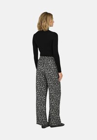 Maglietta nera a maniche lunghe abbinata a pantaloni larghi grigio con stampa leopardata, caratterizzati da una texture morbida e una vita elastica; nessun hardware visibile.