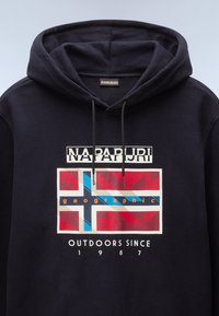 Sudadera navy con capucha ajustable, que presenta un estampado gráfico de una bandera en rojo, blanco y azul, y el texto "Napapijri" y "Outdoors Since 1987."
