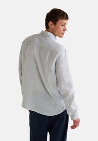 Chemise boutonnée rayée gris clair avec un col, des manches longues et un ourlet arrondi. Fabriquée en tissu texturé, avec de légères lignes verticales.